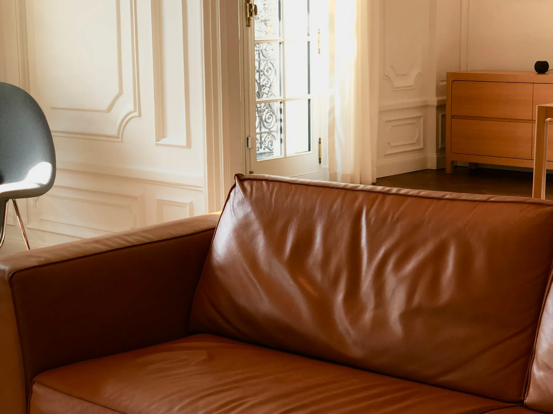 Sofá de piel coñac ante boiserie clásica y balconera con reja de forja